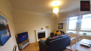 A living room with a fireplace, a sofa, a TV, and a dining table. - Two Bedroom Apartment by Klass Living Serviced Accommodation Airdrie - Nicol Apartment With WiFi & Parking (Airdrie)
