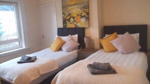 A hotel room with two beds, each with a headboard, pillows, and a blanket. There is a painting on the wall and a window with a view. - Two Bedroom Apartment by Klass Living Serviced Accommodation Airdrie - Nicol Apartment With WiFi & Parking (Airdrie)