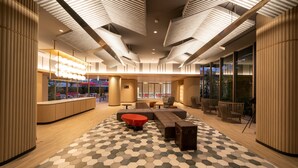 Un moderno hall de hotel con una zona de estar central, una recepción y grandes ventanales con vistas al exterior.