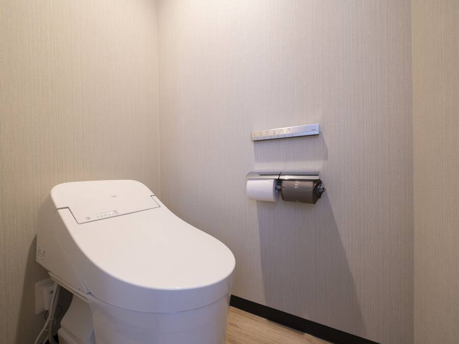 A modern toilet with a control panel, a toilet paper holder, and a measuring scale on the wall.