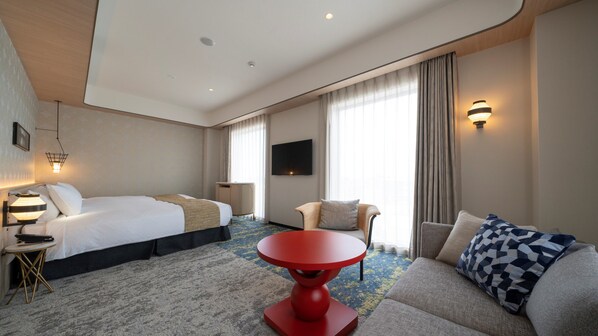 A hotel room with a bed, a sofa, a red table, a TV, and a window with curtains. - Hotel Mu Style Inuyama Experience (Inuyama)