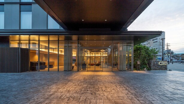 Una entrada de hotel moderna con fachada de vidrio, un área de recepción y un camino de piedra que lleva a la entrada.