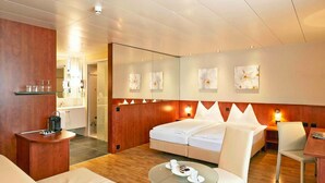 Una habitación de hotel moderna con una cama, una zona de estar con una mesa de vidrio y una pequeña cocina.