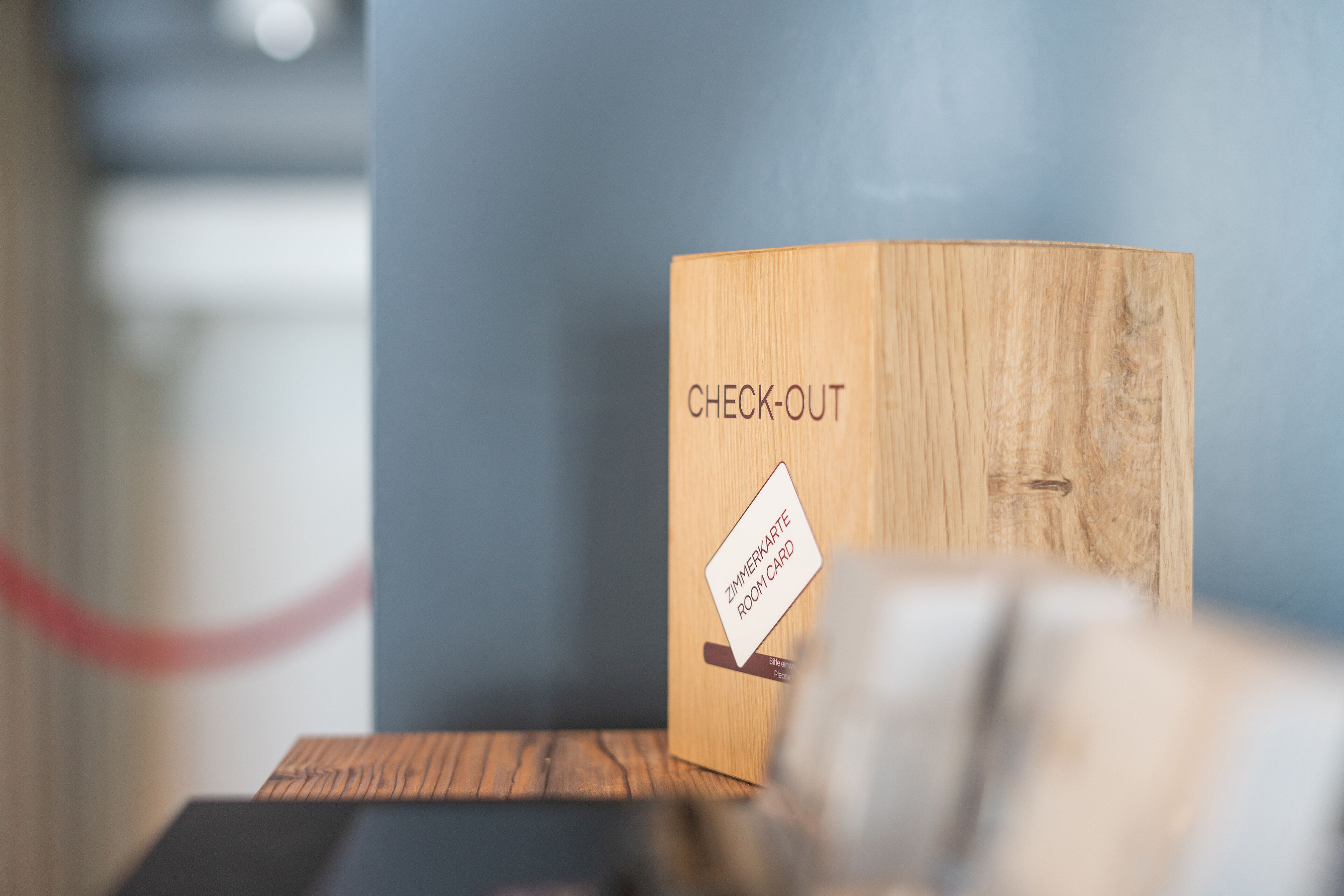 Una caja de madera con la etiqueta 'CHECK-OUT' y un adhesivo que dice 'ZIMMERKARTE ROOMCARD'.