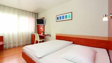 A hotel room with a bed, a desk, a chair, a TV, and a framed picture on the wall.