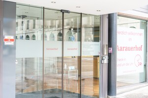 Entrada de hotel con puertas de vidrio, un cartel con los horarios de registro y salida, y un letrero de bienvenida.