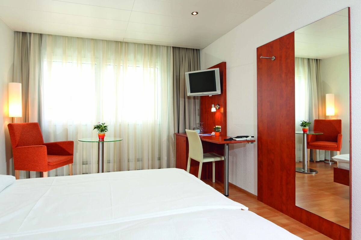 A hotel room with a bed, a desk, two chairs, a TV, and a mirror.