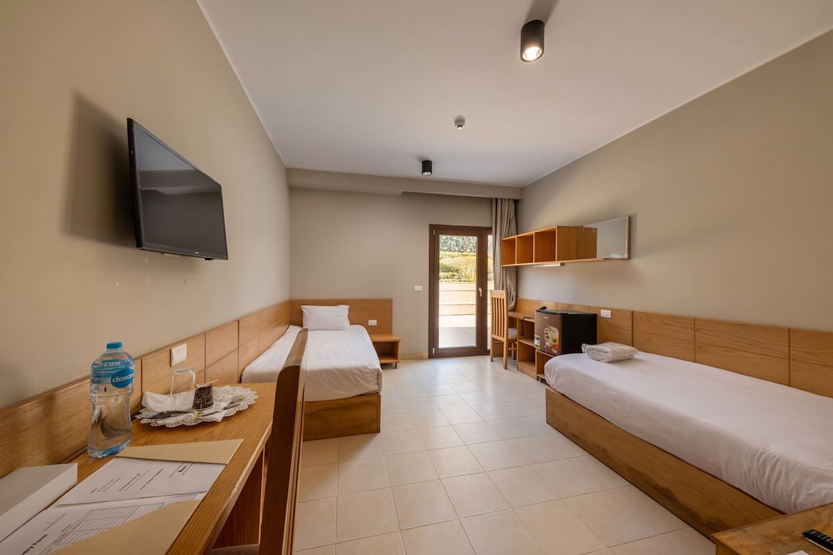 Hotellihuone, jossa on kaksi sänkyä, televisio, työpöytä papereineen ja vesipullo.