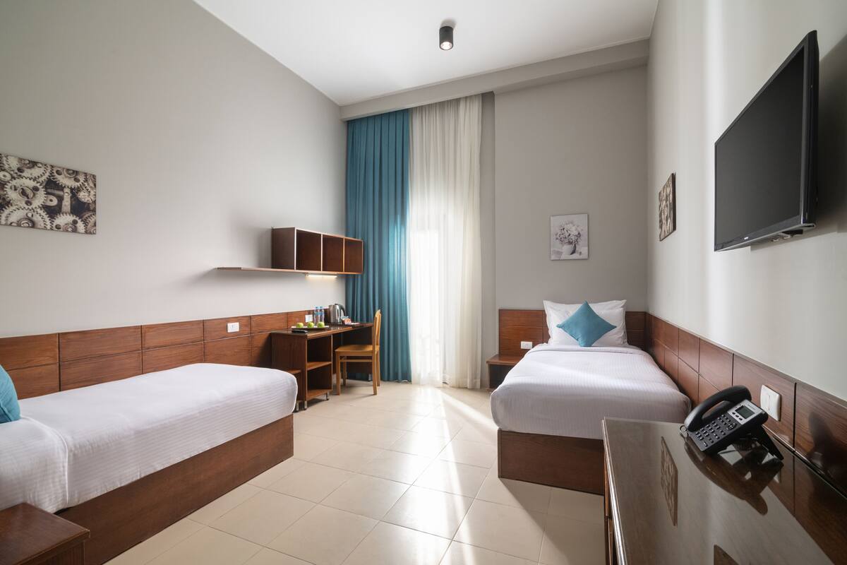 Hotellihuone, jossa on kaksi erillistä sänkyä, työpöytä, tuoli, televisio ja puhelin.