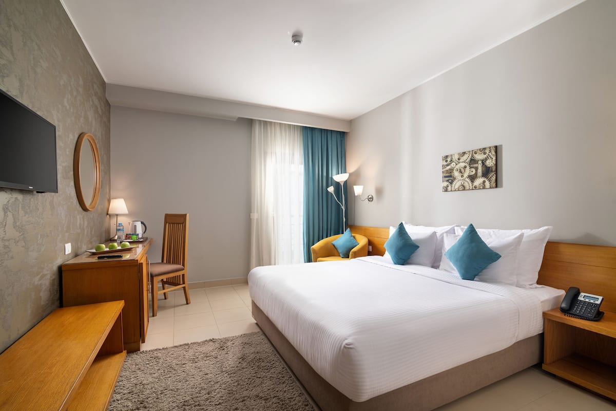 Hotellihuone, jossa on suuri sänky, työpöytä tuolilla, pieni pöytä, televisio ja taulu seinällä.