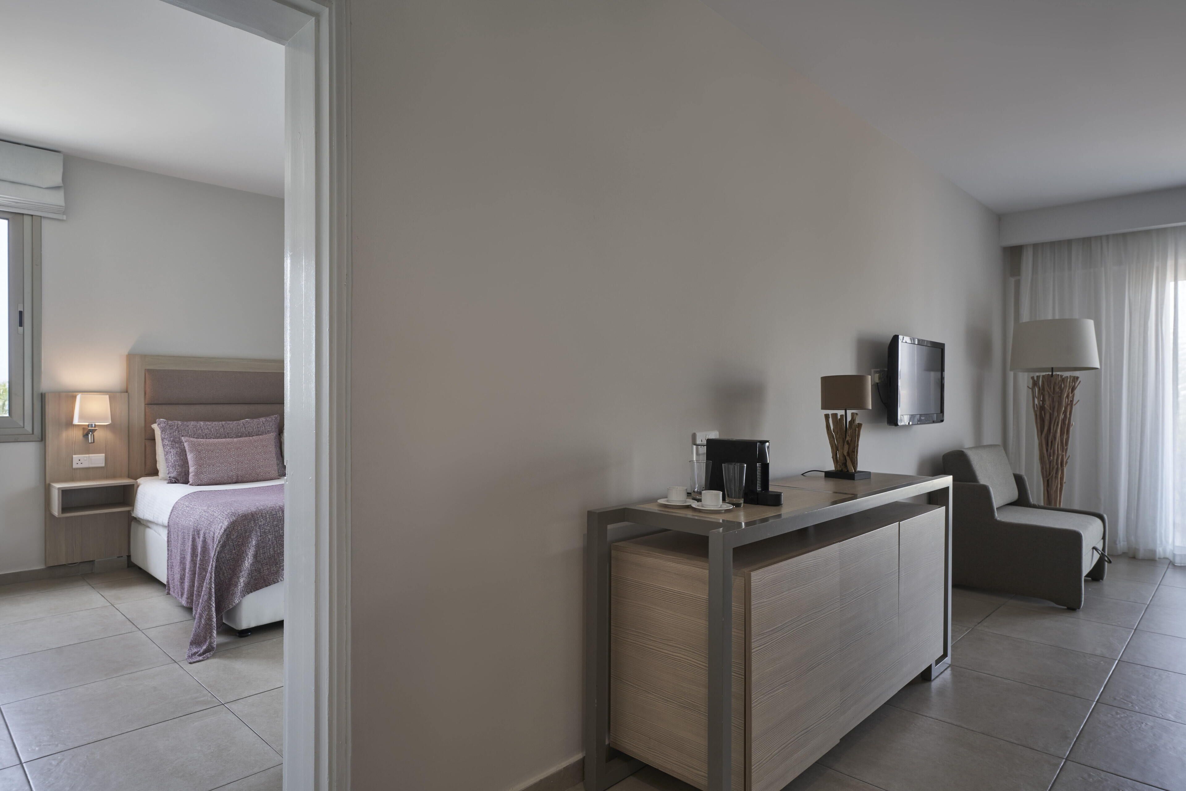 Ein modernes Hotelzimmer mit Bett, Nachttisch, Lampe, Fernseher und Schreibtisch mit Stuhl.