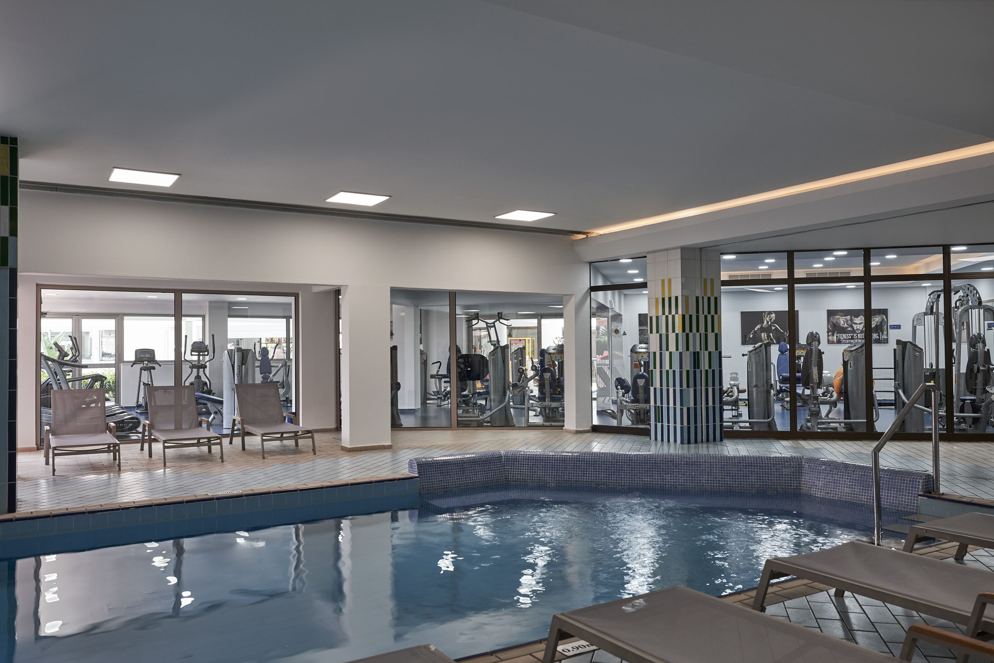 Ein Hallenbad mit Fitnessgeräten und Liegestühlen.