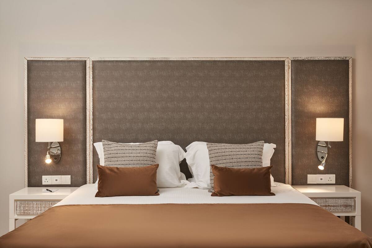 A neatly made bed with brown bedding, two bedside lamps, and a textured headboard.
