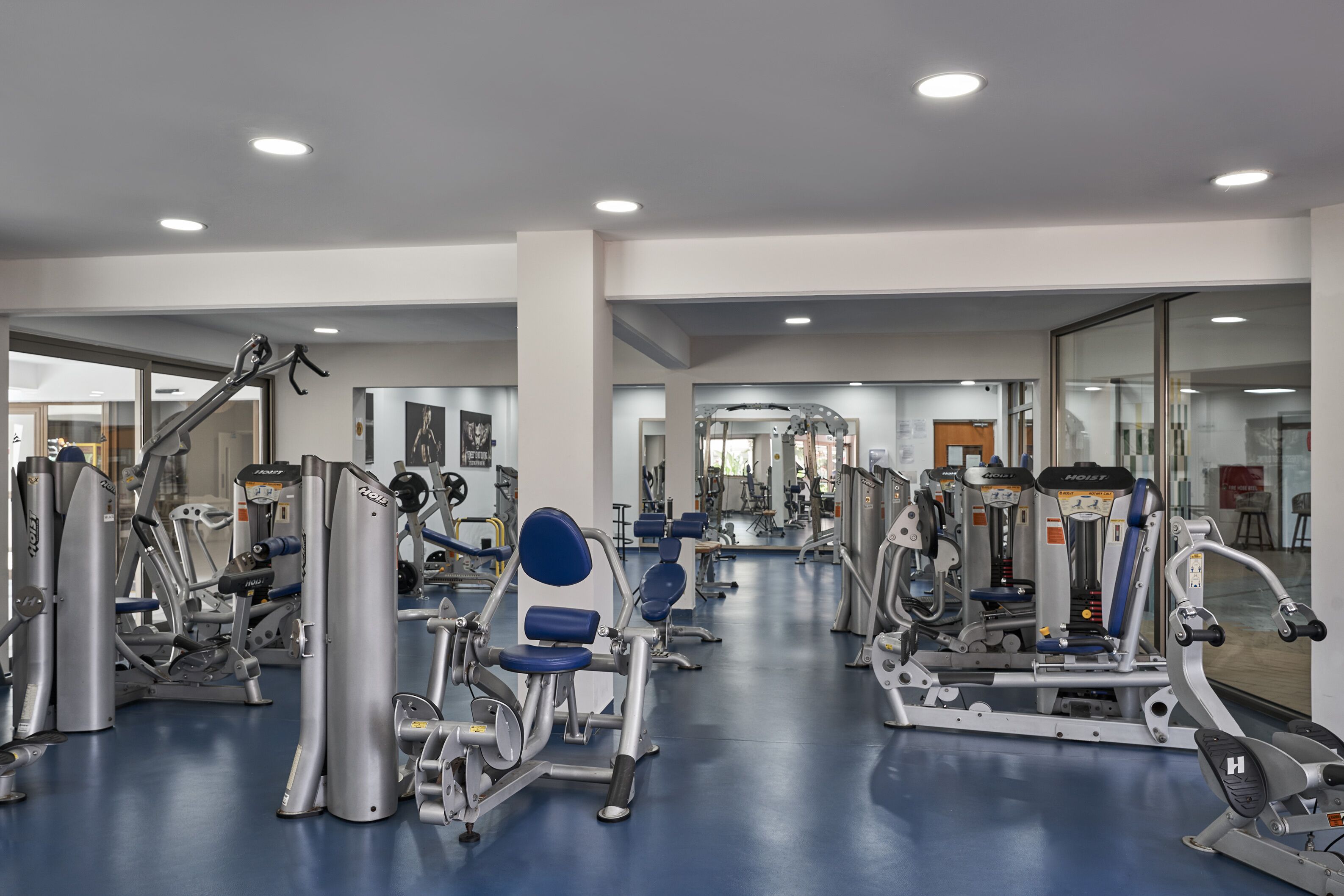 Uma academia com diversos equipamentos de exercício, espelhos e piso azul.