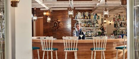 Un espace bar avec un comptoir en bois, des tabourets de bar blancs et un barman.
