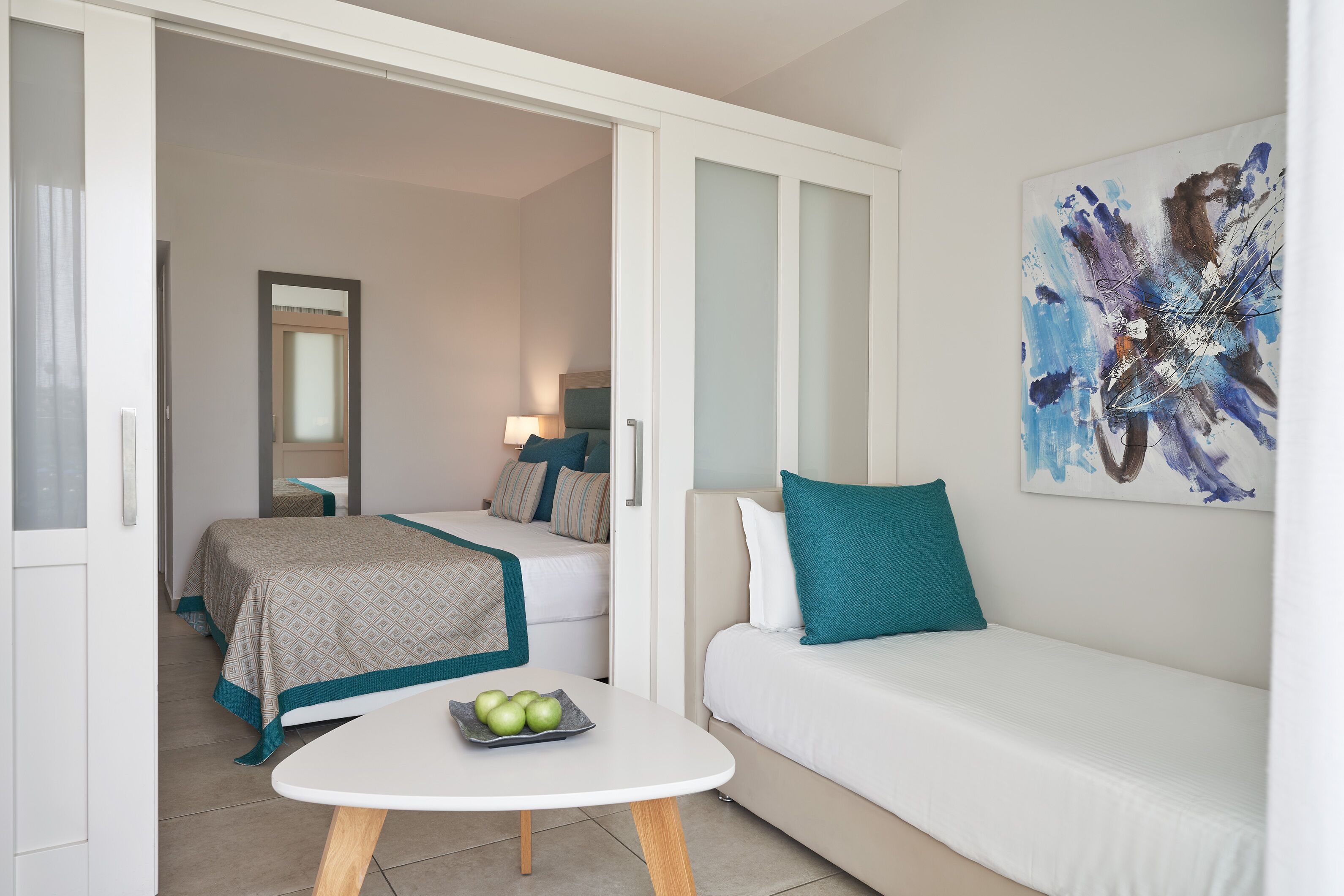 A modern hotel room with a bed, a sofa, and a small table with apples.