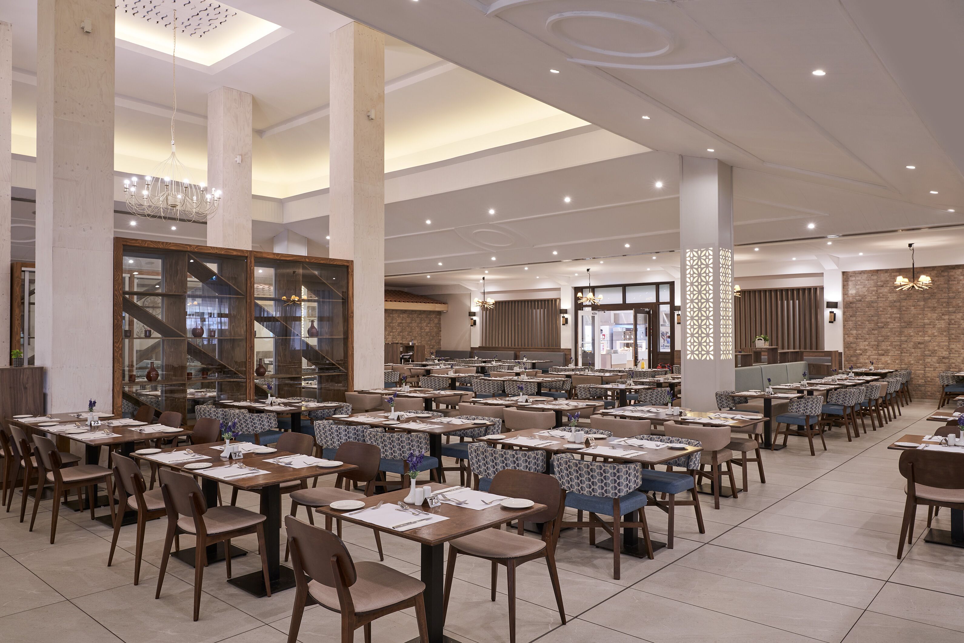 A spacious dining area with multiple tables and chairs, large pillars, and a modern ceiling design.