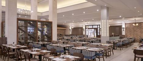 A spacious dining area with multiple tables and chairs, large pillars, and a modern ceiling design.