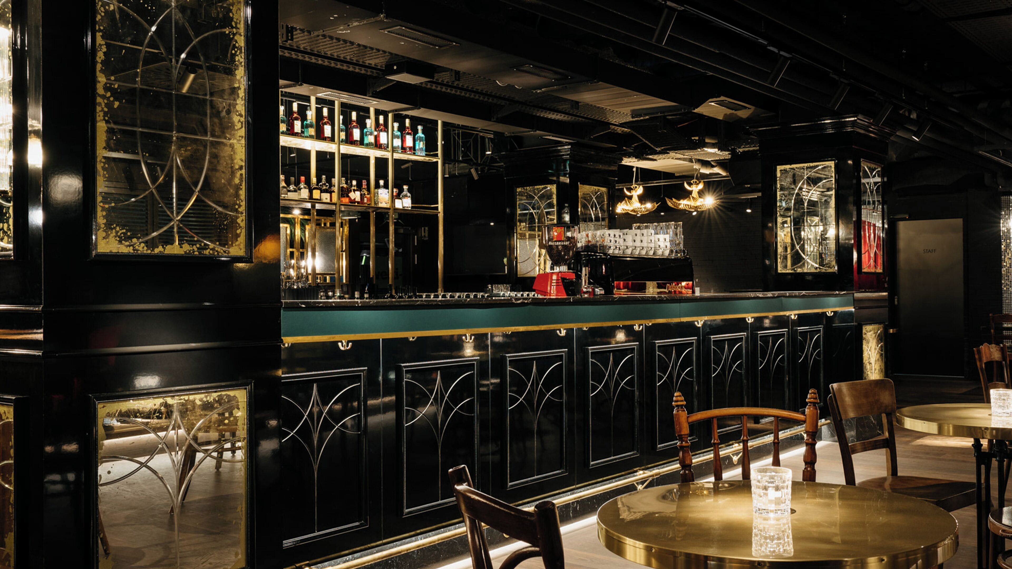 A bar area with a counter, shelves of bottles, and a seating area with tables and chairs.