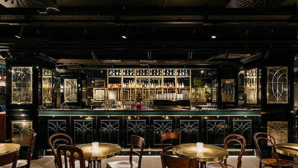 A bar area with multiple tables and chairs, a counter with bottles, and decorative glass panels. - Ruby Mimi Hotel Zurich by IHG (Zürich)