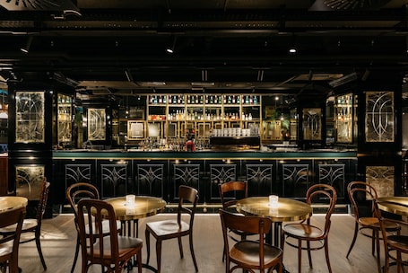A bar area with multiple tables and chairs, a counter with bottles, and decorative glass panels.