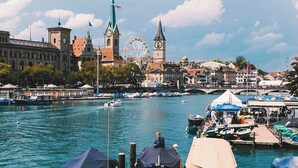 A river with boats, a Ferris wheel, and historic buildings in the background. - Ruby Mimi Hotel Zurich by IHG (Zürich)