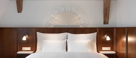 Una habitación de hotel con una cama grande, dos mesitas de noche con lámparas, un cabecero de madera y un adorno decorativo sobre la cama.