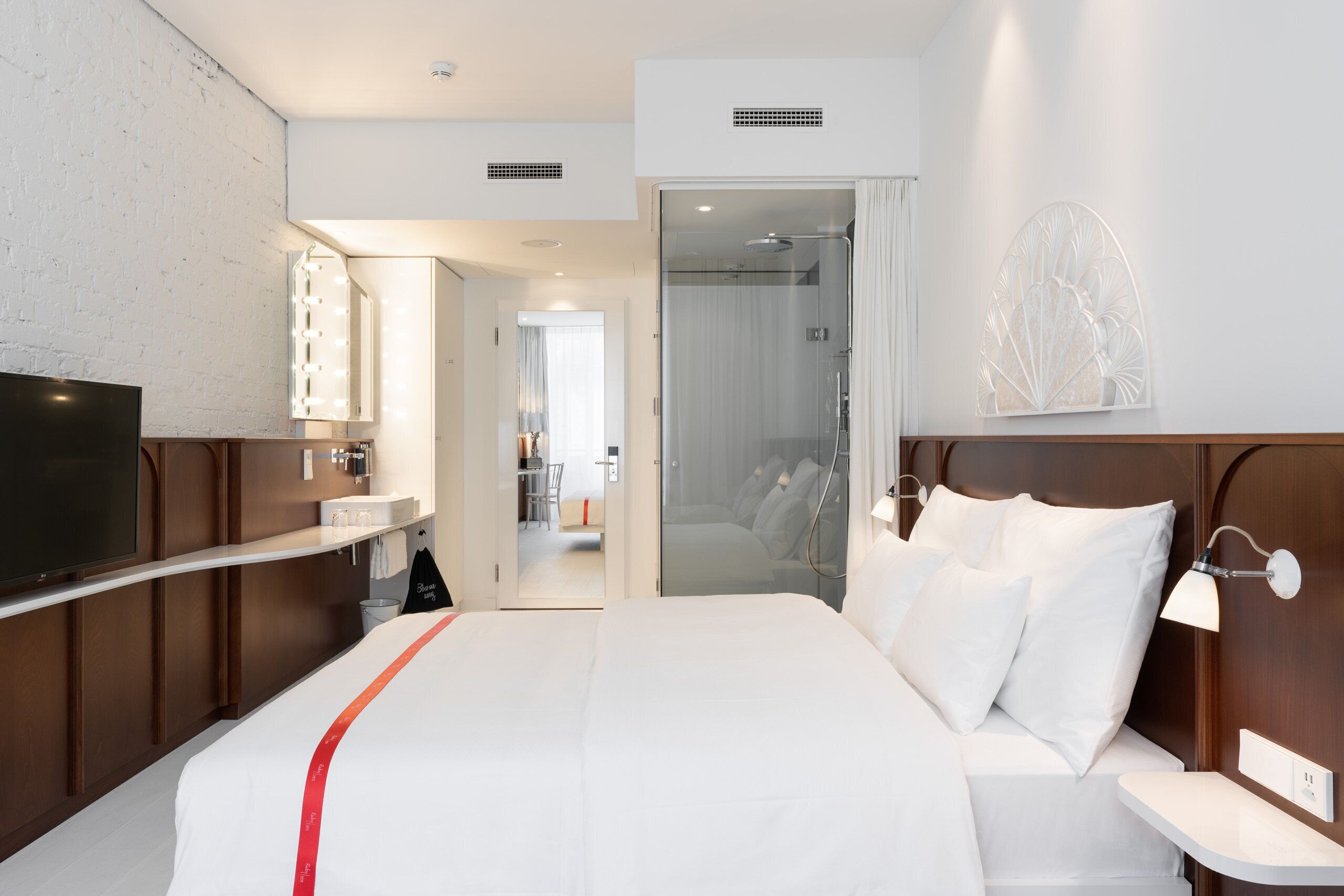 Une chambre d’hôtel comprenant un lit, une télévision, une salle de bain avec douche et un couloir menant à une autre pièce.
