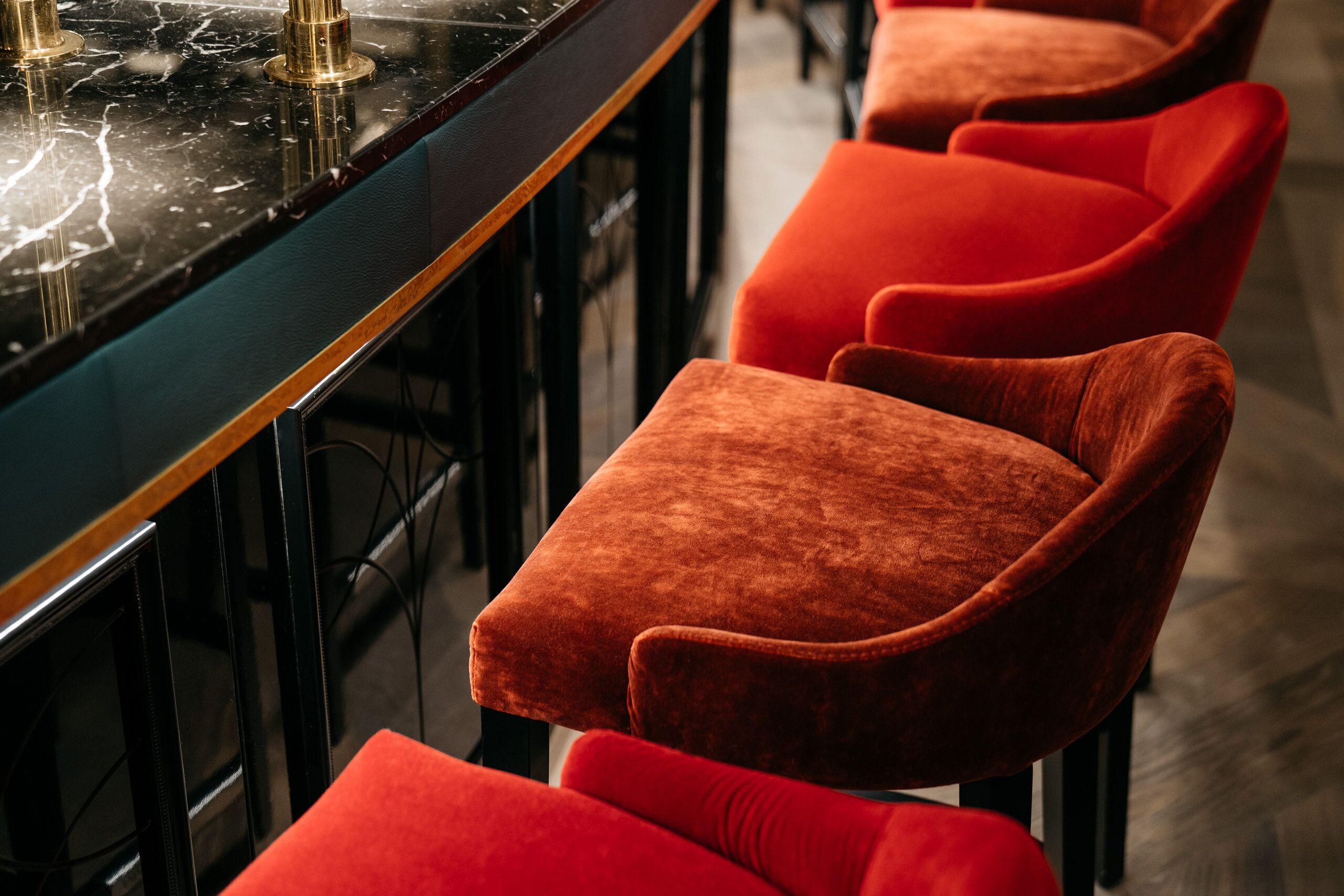 Una zona de bar con encimera de mármol negro y sillas de terciopelo rojo.