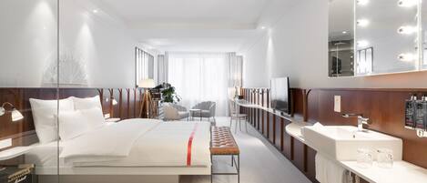 Una habitación de hotel moderna con una cama grande, un tocador con espejo y una zona de estar con sillas.