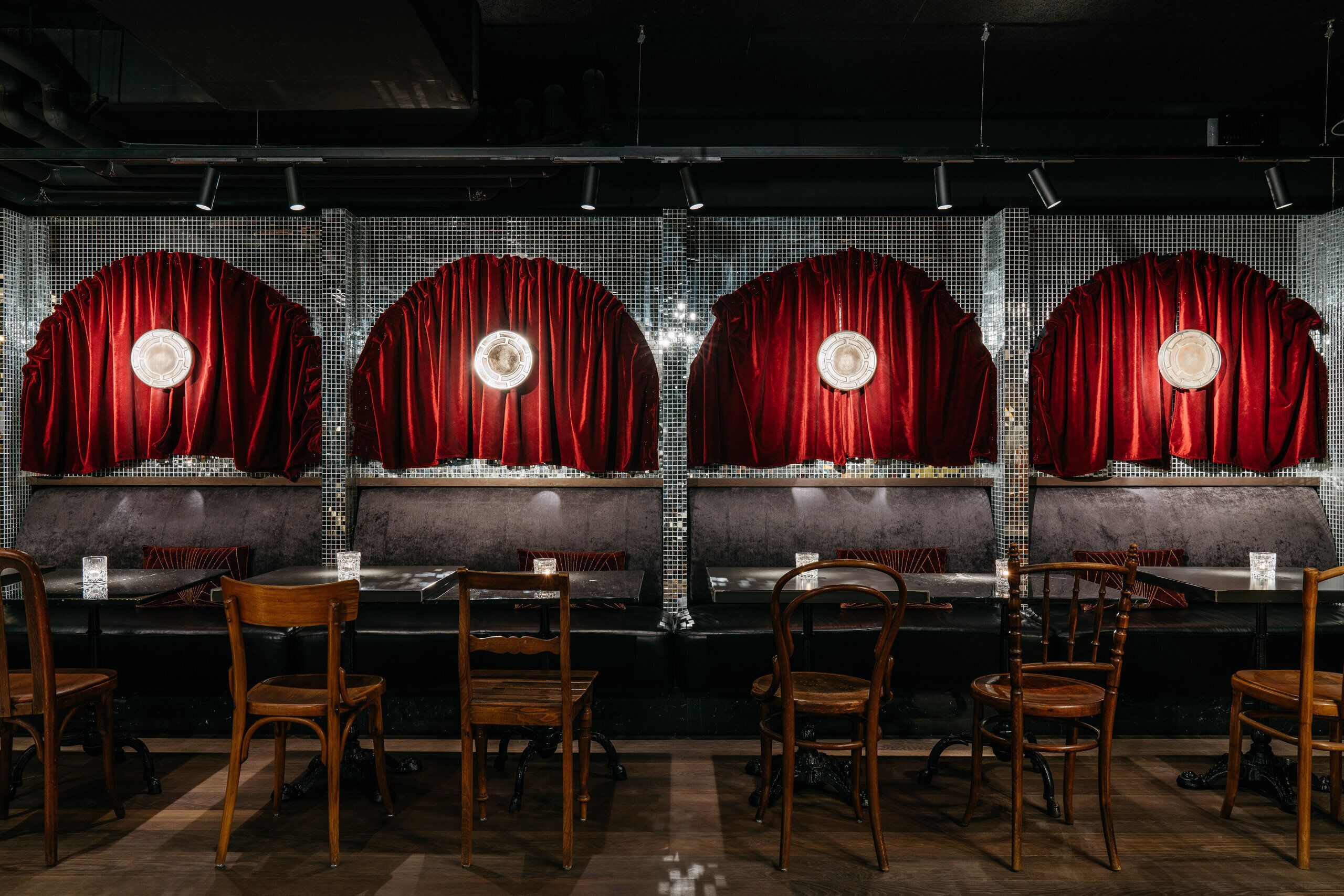 A restaurant interior with a long counter, four red curtains, and wooden chairs.
