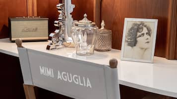 A vintage radio, a glass jar, a framed picture, and a chair labeled 'MIMI AGUGLIA' on a white table.