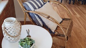A wicker chair with striped cushions, a white table with a potted plant, and a white lantern. - Recently renovated house in quiet leafy surroundings..  (Warrnambool)