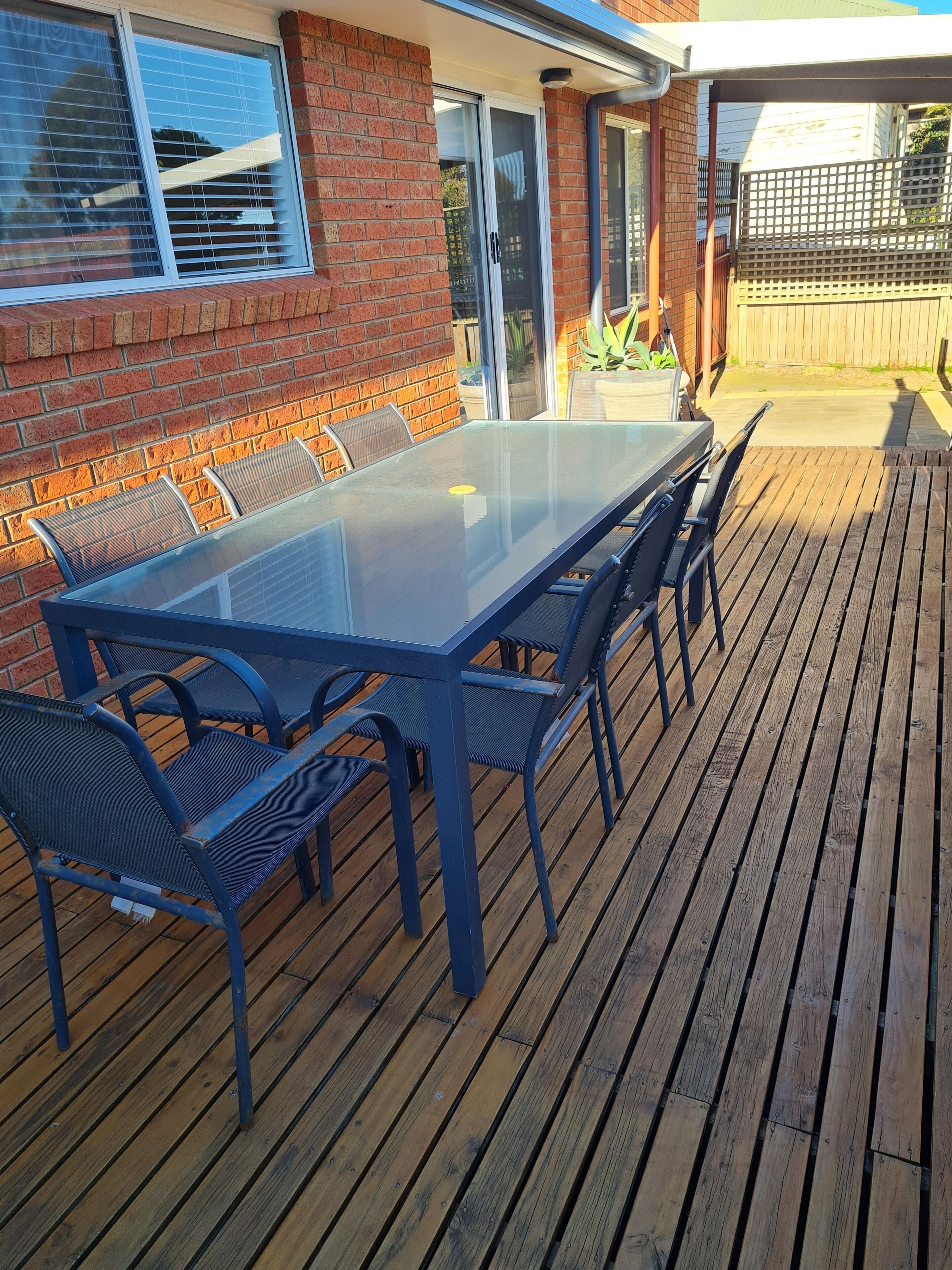 A glass-top table with blue metal chairs on a wooden deck.