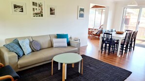 A living room with a sofa, a round table, and a dining area with chairs and a table. - Recently renovated house in quiet leafy surroundings..  (Warrnambool)