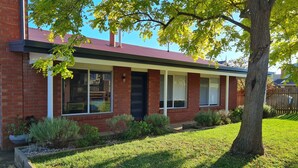 A two-story brick house with a covered porch, a well-maintained lawn, and a tree in the foreground. - Recently renovated house in quiet leafy surroundings..  (Warrnambool)