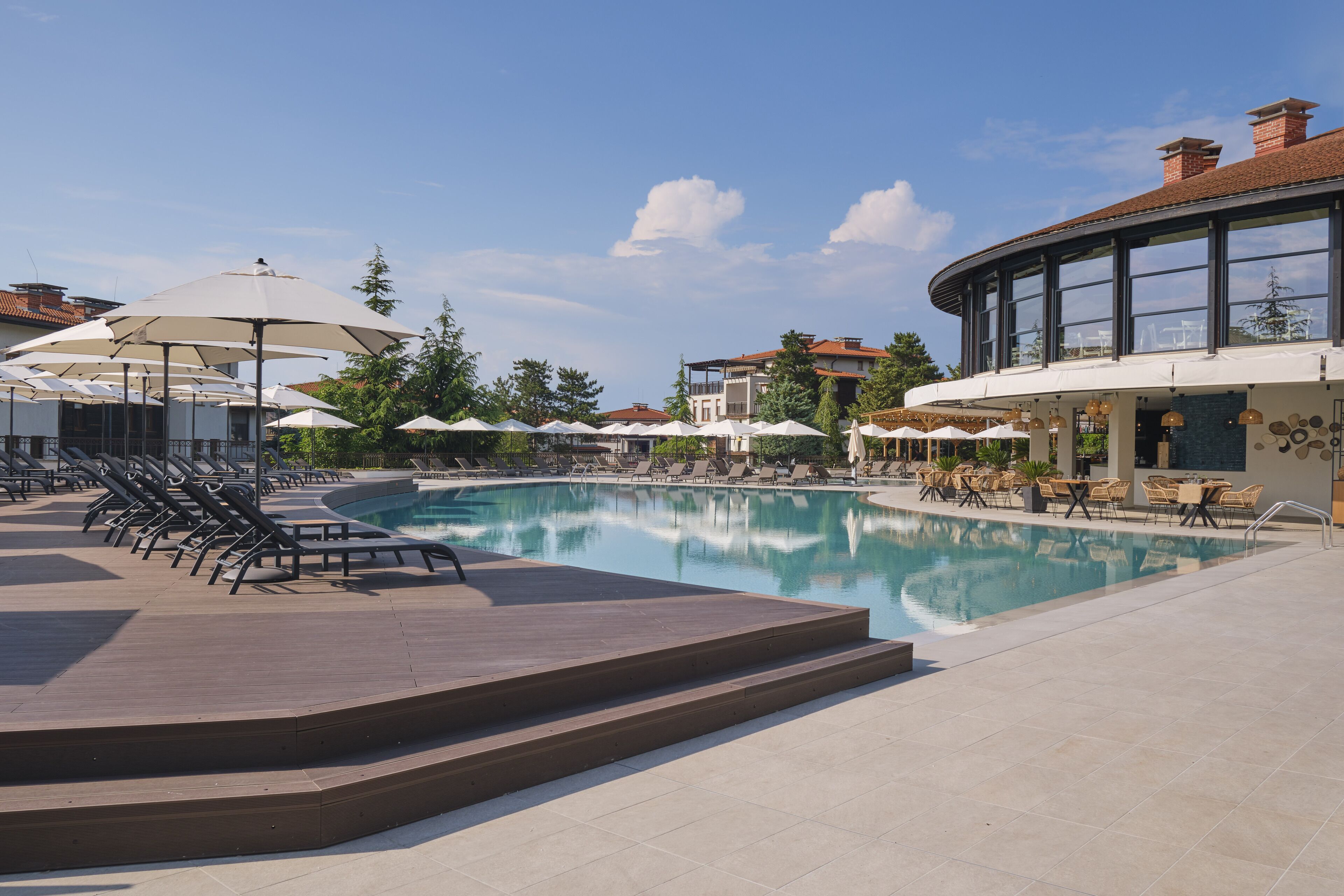 A pool area with lounge chairs and umbrellas, a clear sky, and a building with large windows.
