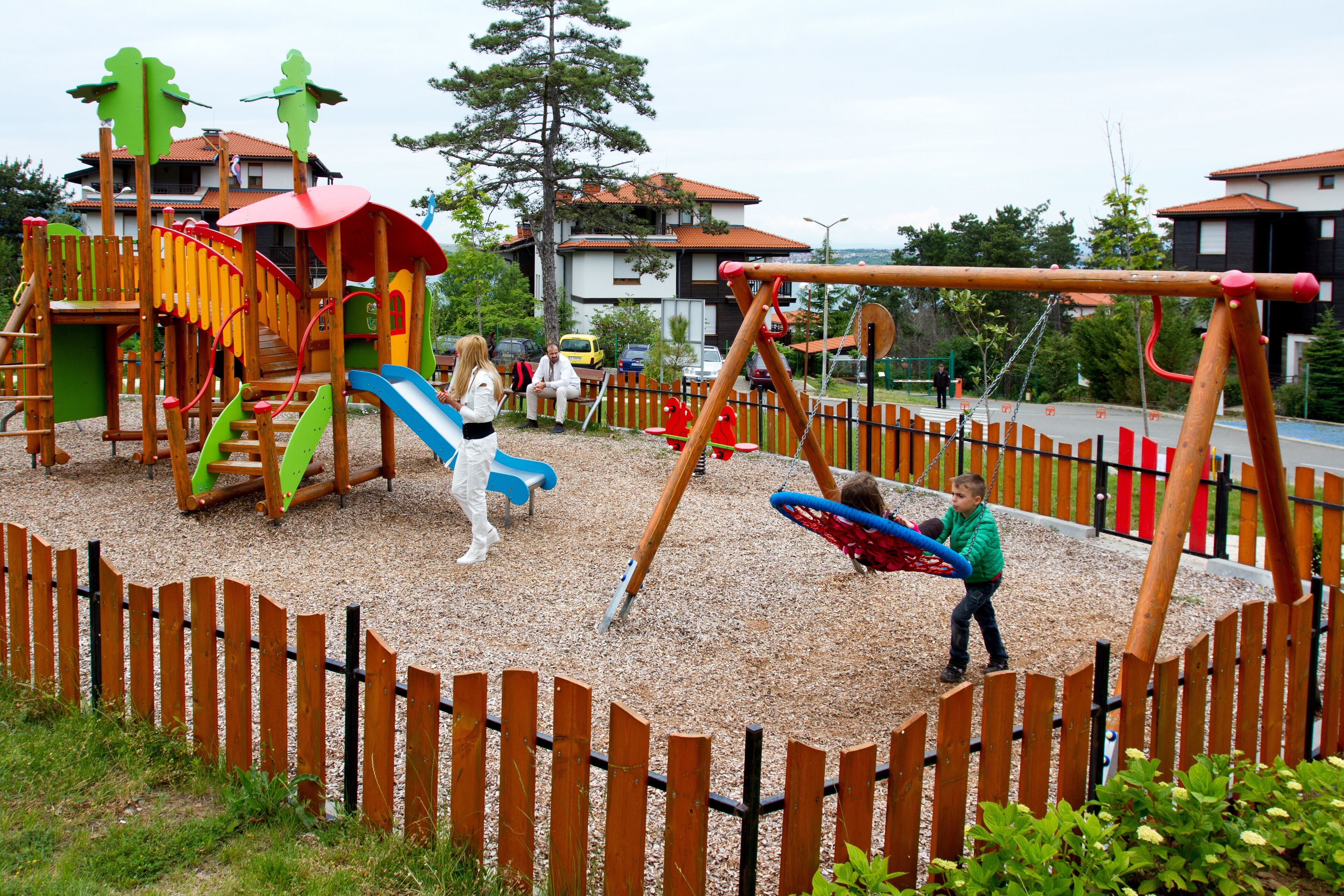 A playground with various play structures, including slides and swings, surrounded by a wooden fence.