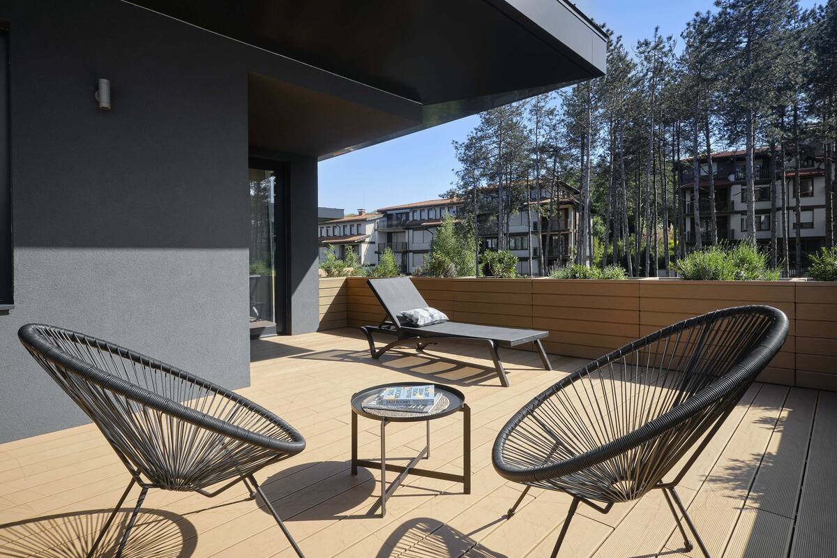 Un patio moderno al aire libre con dos sillones, una mesita y vistas a edificios residenciales y árboles.