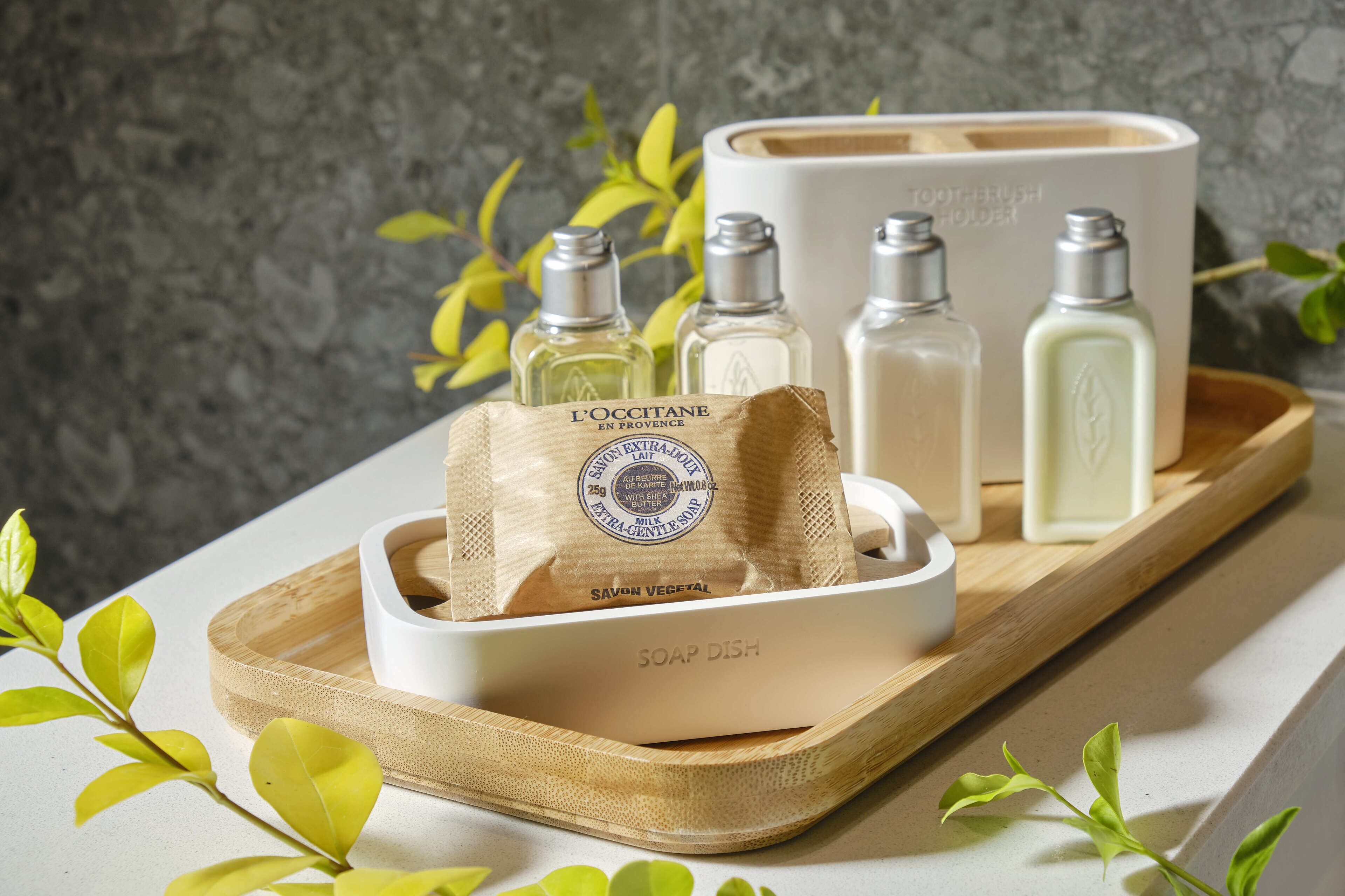A tray with soap bottles and a soap dish on a wooden tray, with a box labeled "TOOTHBRUSH HOUSE" in the background.