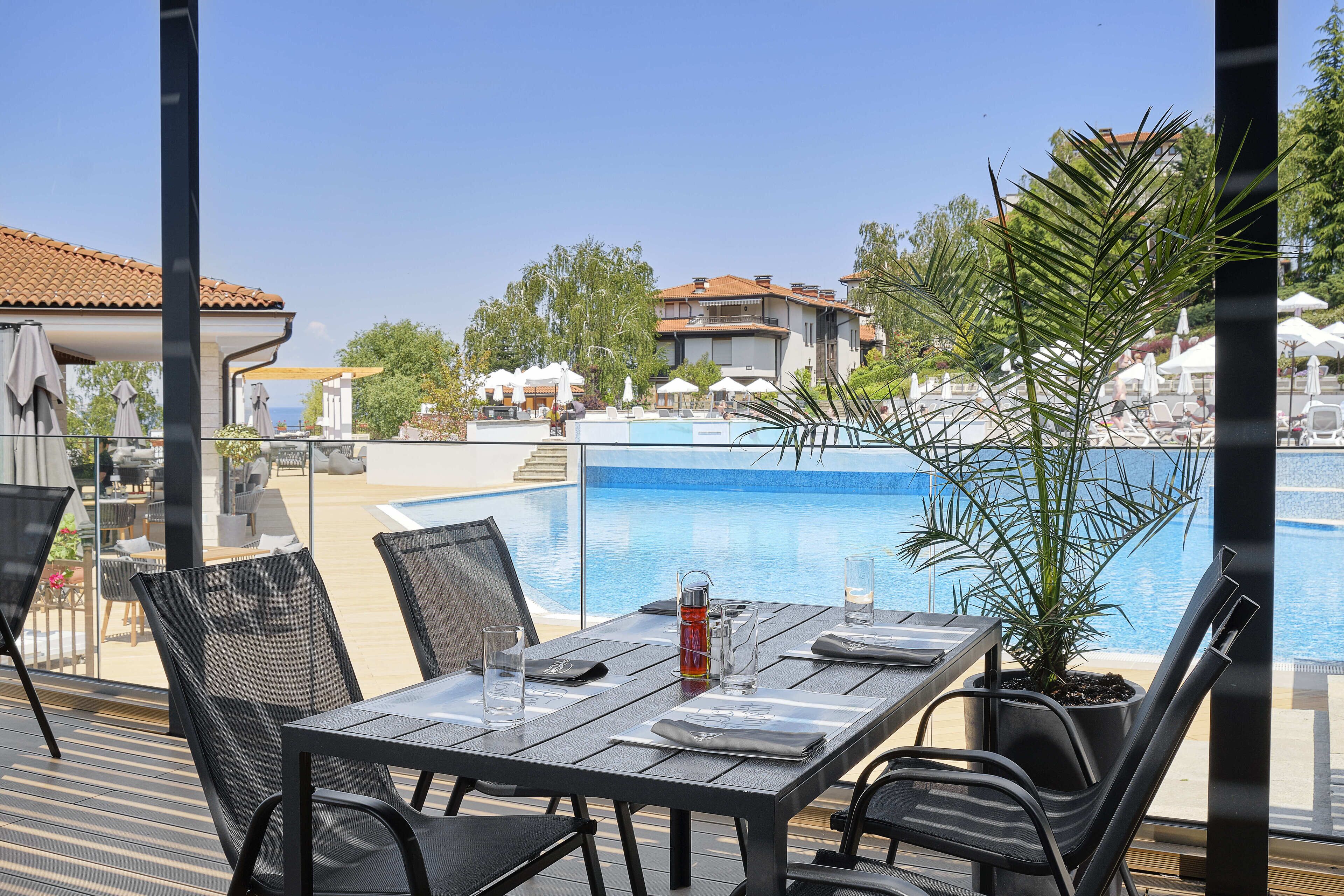 An outdoor dining area with a pool view, including tables, chairs, and a potted plant.