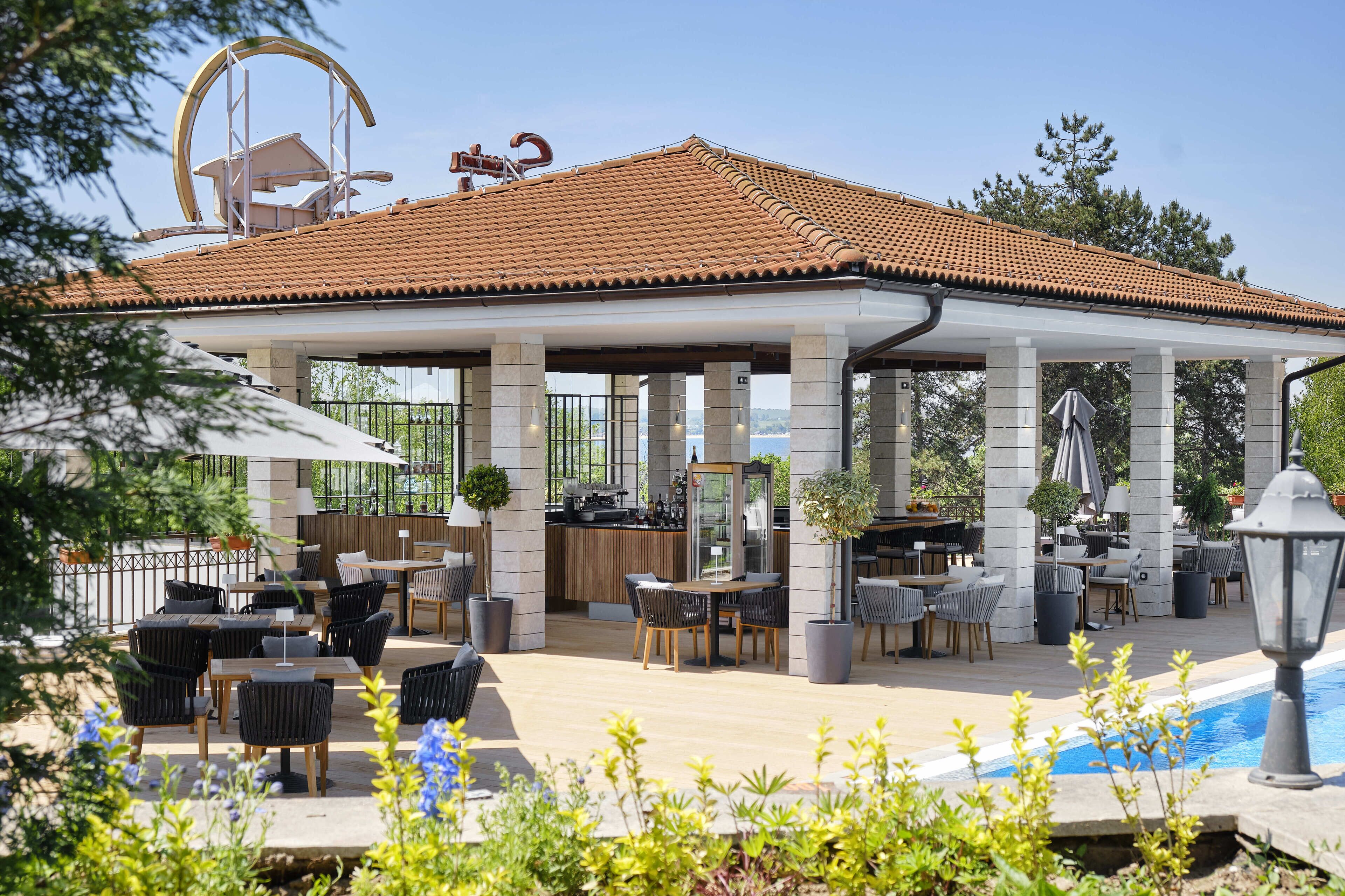 Un área de estar al aire libre con techado, mesas, sillas, piscina y bar.