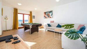 A modern living room with a pool table, sofa, and a large plant.
