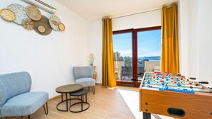 A room with a foosball table, two sofas, a small table, and a window with curtains.