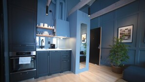 A modern kitchen with dark cabinetry, a built-in oven, and a sink. There is a wooden floor and a potted plant in the corner. - Home Again Kirkegata 30 (Stavanger)