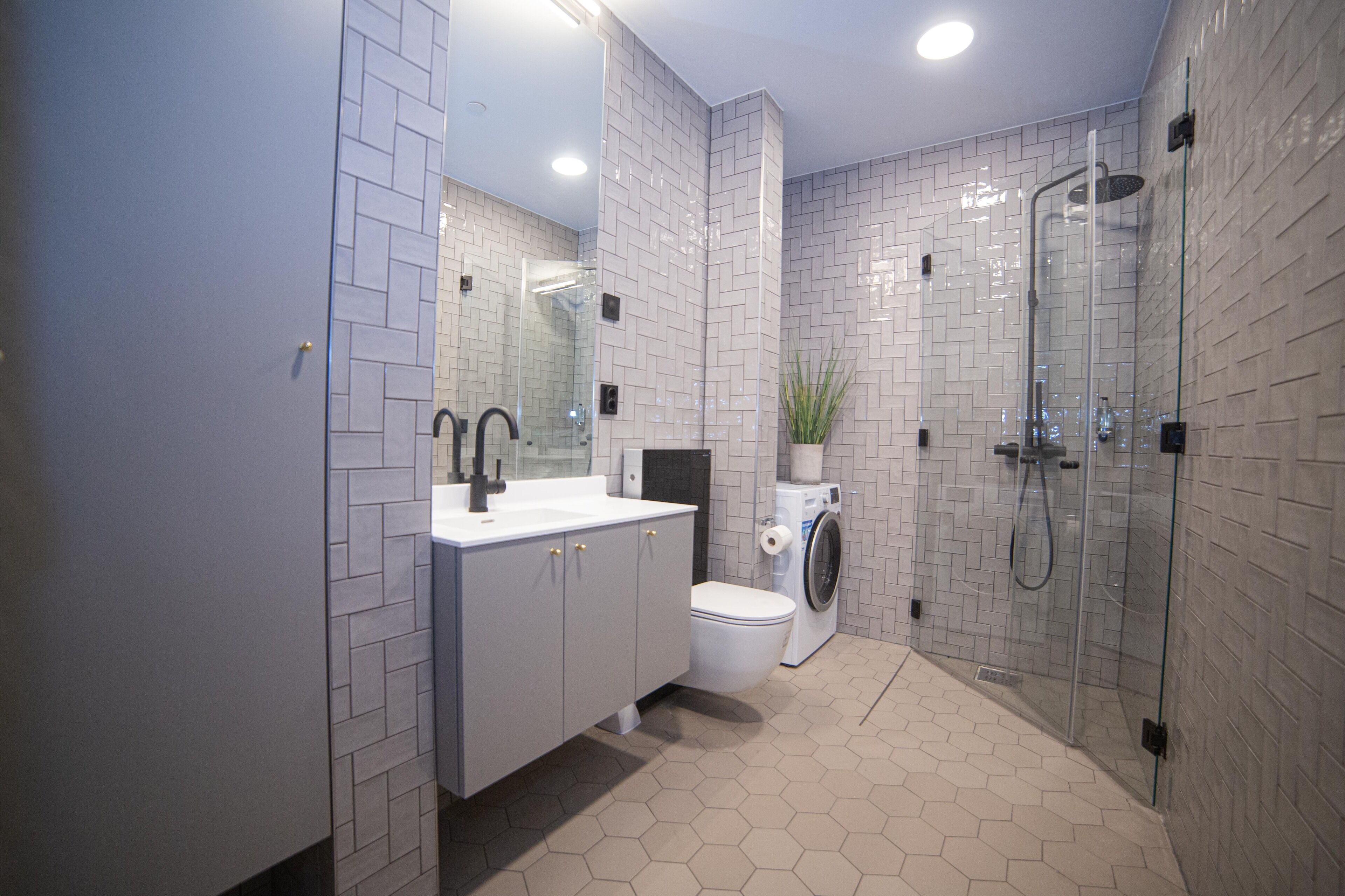Ein modernes Badezimmer mit einer Duschkabine, Toilette, Waschmaschine und Waschbecken mit Spiegel.