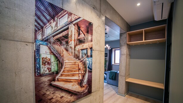 A hallway with a large mural of a staircase, wooden shelves, and a tiled floor. - Home Again Kirkegata 30 (Stavanger)