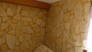 Ein Zimmer mit einer Steinsäule, Holzbalkendecke und Fliesenboden, sowie einem Sofa mit gemustertem Bezug.