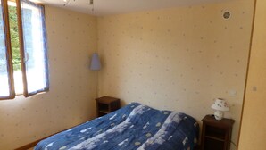 Ein Schlafzimmer mit einem Bett, einem Nachttisch, einer Lampe und einem Fenster mit Vorhängen.