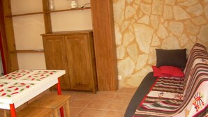 Ein Zimmer mit einer Steinwand, Holzmöbeln, einem Tisch mit kariertem Tischtuch und einem Sofa mit bunter Decke.